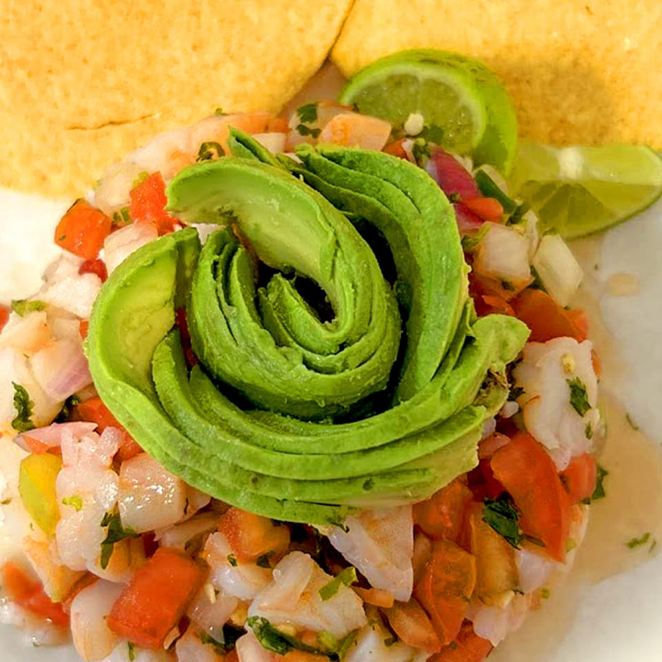 Shrimp ceviche with diced tomatoes, onions, cilantro, avocado, lime wedges, and tortilla chips.