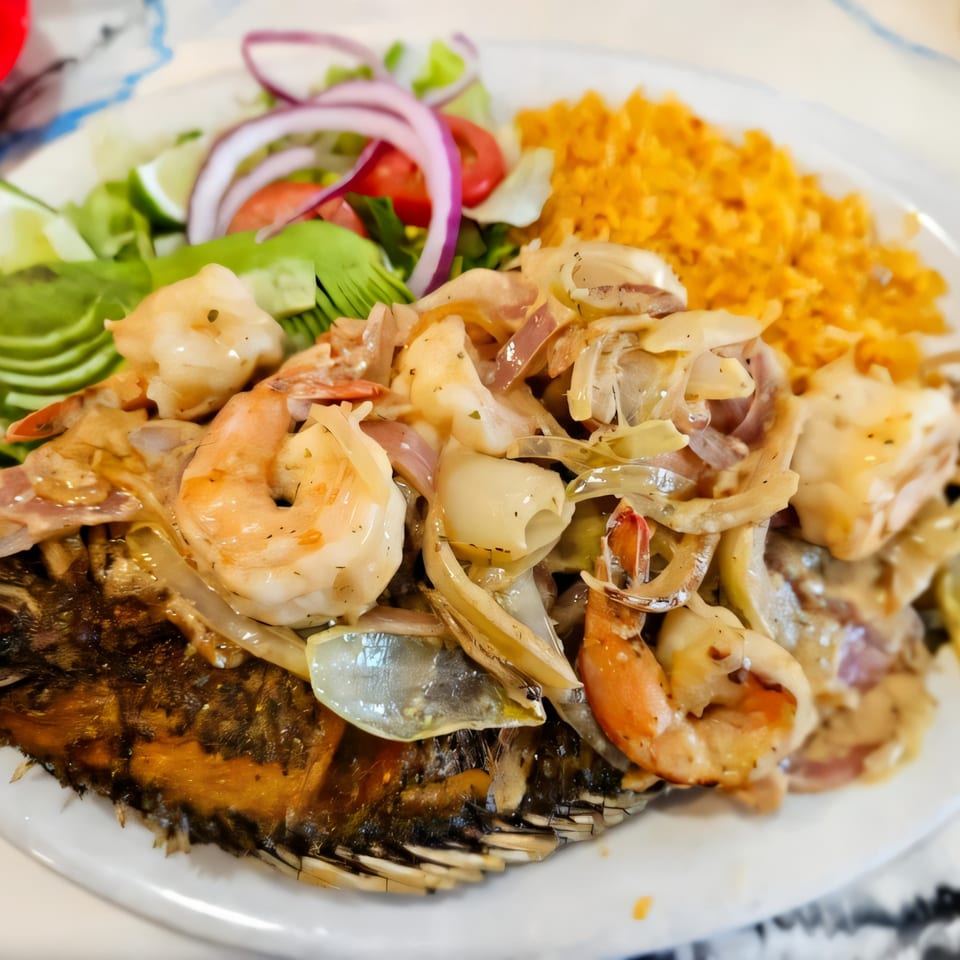 Whole fried fish topped with shrimp, onions, and sauce, served with rice and salad.