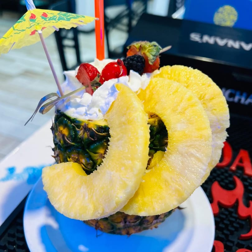 A pineapple drink with whipped cream, berries, pineapple slices, and a small umbrella.