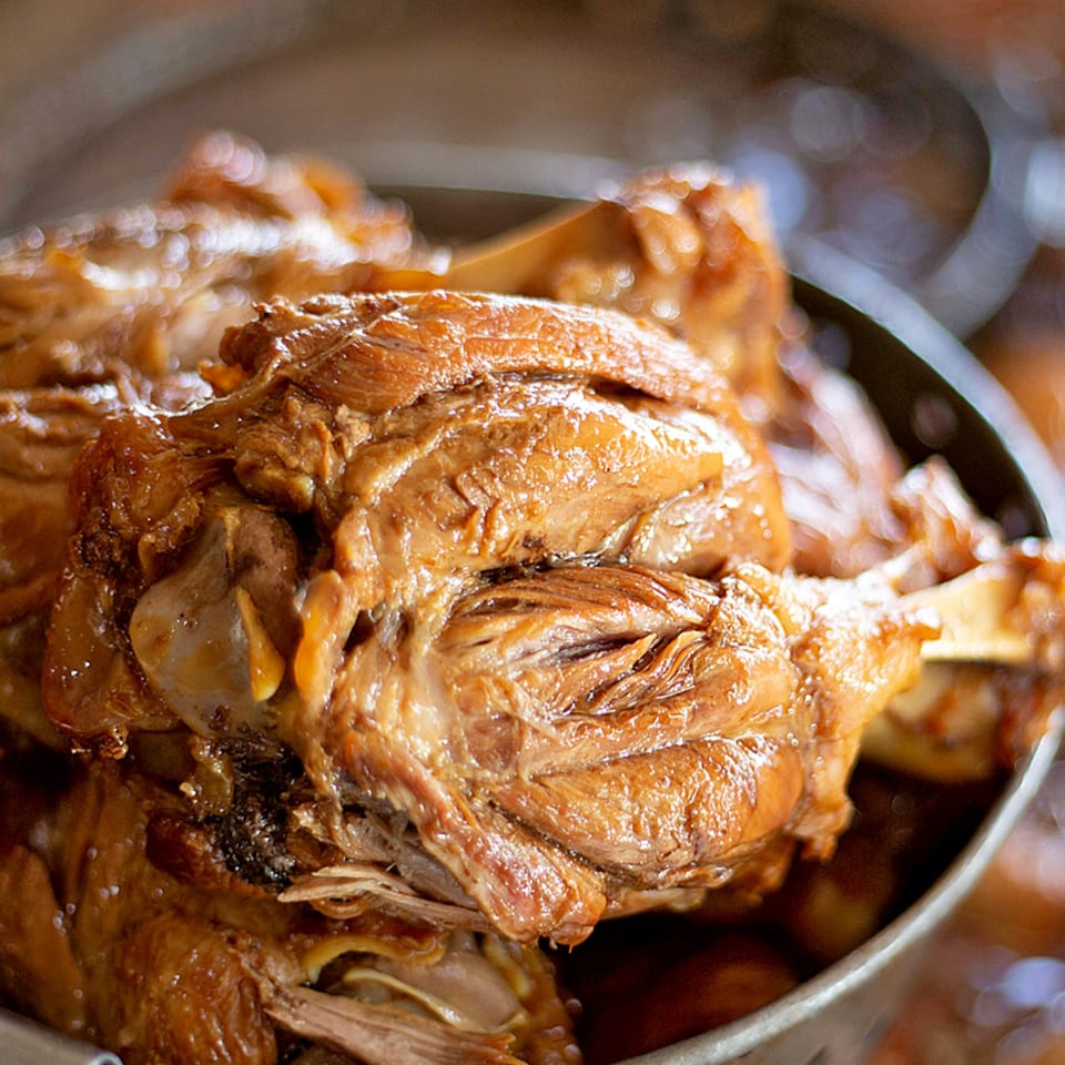 Close-up of tender, braised Mexican pork shank, glistening with sauce in a metal pot.