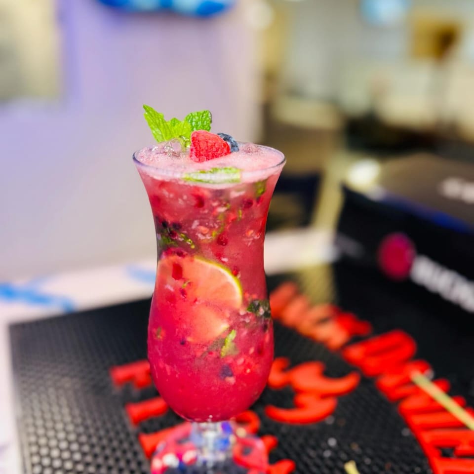 A vibrant red berry mojito, garnished with mint and lime, sits on a dark textured surface.